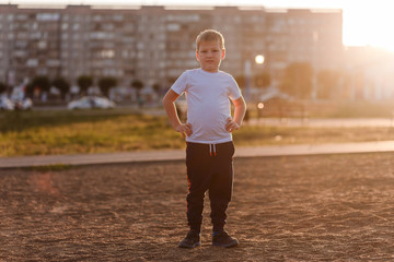 seven-year-old boy in a white t-shirt in full growth looking at the camera in the sunset light in the city .