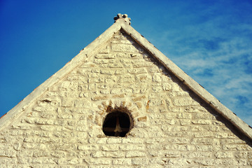 Fototapeta na wymiar The triangular roof of an old building of yellow stone against a blue sky