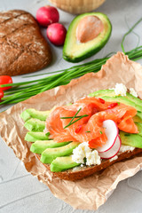 sandwich with avocado and salmon on a light background, green onions and gluten-free grain bread, radishes and tomatoes. concept diet food, copy space, sandwich take away, healthy fast food