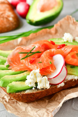 sandwich with avocado and salmon on a light background, green onions and gluten-free grain bread, radishes and tomatoes. concept diet food, copy space, sandwich take away, healthy fast food