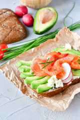 sandwich with avocado and salmon on a light background, green onions and gluten-free grain bread, radishes and tomatoes. concept diet food, copy space, sandwich take away, healthy fast food