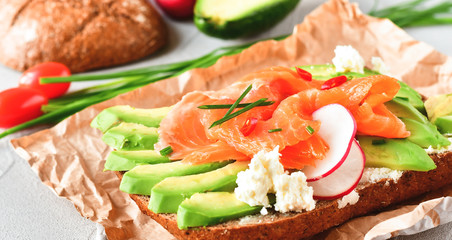 sandwich with avocado and salmon on a light background, green onions and gluten-free grain bread, radishes and tomatoes. concept diet food, copy space, sandwich take away, healthy fast food