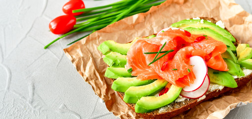 sandwich with avocado and salmon on a light background, green onions and gluten-free grain bread, radishes and tomatoes. concept diet food, copy space, sandwich take away, healthy fast food