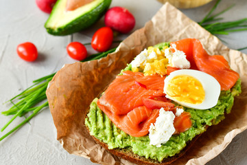 sandwich with avocado and salmon on a light background, green onions and gluten-free grain bread, radishes and tomatoes. concept diet food, copy space, sandwich take away, healthy fast food