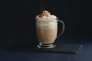 Coffee and milk latte drink with whipped cream, nuts and cocoa powder. Sweet hot drink on a dark background with copy space for a menu