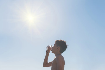 Silhouette of teen boy with glass of juice on the beach opposite sun. Concept