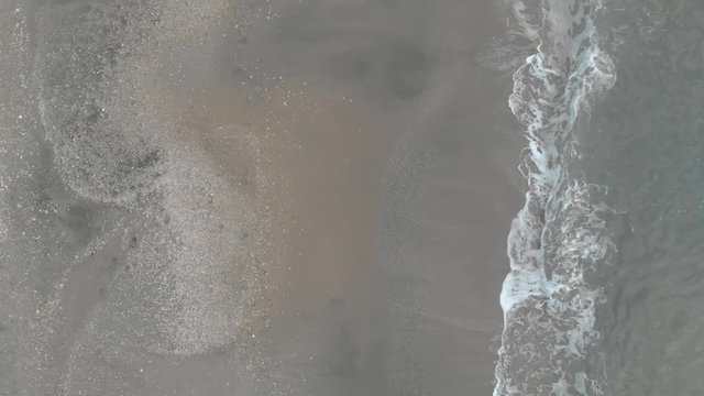 Aerial flat-lay view over  motion ocean surface and its undertow with emerald colored water crashing on the sand with a lot of  white foam