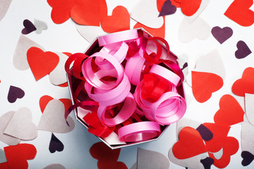 Festive decorations. Red and pink ribbons in a box on a white background. Nearby lay colored paper hearts. Celebration concept.