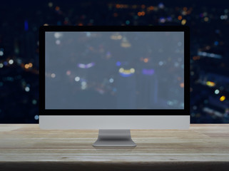 Desktop modern computer monitor with wide screen on wooden table over blur colorful night light city tower and skyscraper