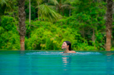 young attractive and beautiful Asian Chinese woman relaxing happy at tropical beach resort swimming at jungle infinity pool enjoying Summer holidays in paradise island