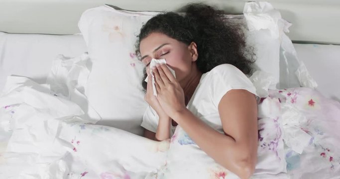 Sick woman lying on bed and sneezing on a tissue in bedroom at home. Shot in 4k resolution