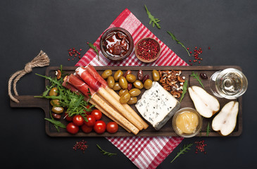 Mediterranean products (ham, blue cheese, arugula, cherry, nuts) on a brown cutting board. Dark background. Useful natural fresh food