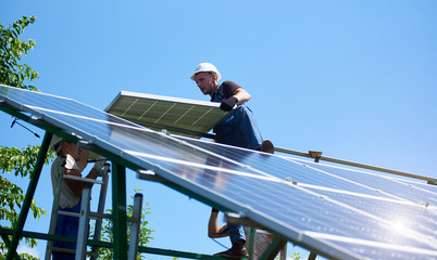 Professional workers team installing solar panels on the green metal construction using different...