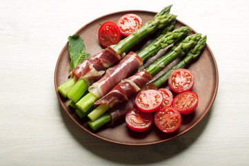 Asparagus with ham and tomatoes in a plate on a white surface. Delicious and hearty dish.