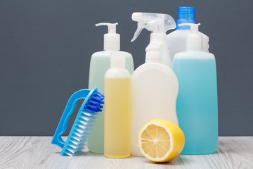 Bottles of dishwashing liquid, brush and lemon on gray background.