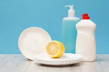 Bottles of dishwashing liquid, plates and lemon on blue background.
