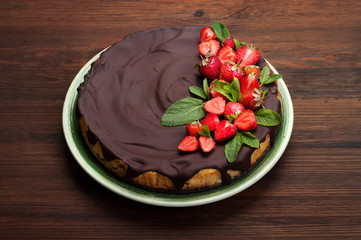 Cheesecake (homemade cake), poured with chocolate icing, with strawberry berries in a plate (side view). Sweets on a brown wooden board. Organic product. Place for text