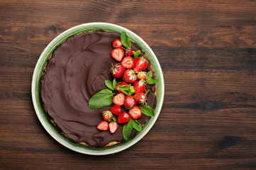 Cheesecake (homemade cake), poured with chocolate icing, with strawberry berries in a plate. Sweets on a brown wooden board. Organic product. Place for text