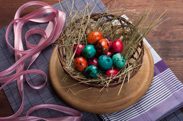 Pink, orange and green quail eggs on the hay in the basket on a violet mat.  Brown wooden background.  Concept Easter food