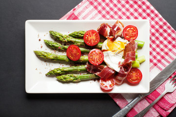 Asparagus with spices and egg poached in a white plate on a dark background. Light diet breakfast