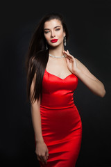 Glamorous model in red silky dress. Perfect brunette woman with makeup and diamond necklace on black background