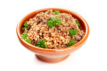 Cooked buckwheat in a rustic earthenware bowl, garnished with fresh parsley, on a white background with a place for text