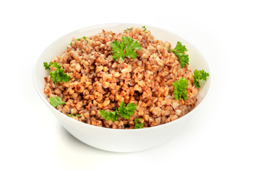 Cooked buckwheat in a bowl, garnished with fresh parsley, on a white background with a place for text