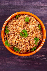 A photo of buckwheat in a rustic earthenware bowl, garnished with fresh parsley, shot from the top on a dark wooden background with a place for text
