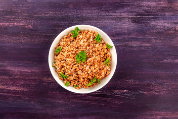 Cooked buckwheat in a rustic earthenware bowl, garnished with fresh parsley, shot from above on a dark wooden background with a place for text