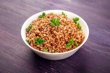 Cooked buckwheat in a bowl, garnished with fresh parsley, on a purple background with copy space