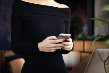 Female hands holding mobile phone checking online messages or corporate cell, business woman using mobile applications on smartphone in office with laptop, typing message, close up view