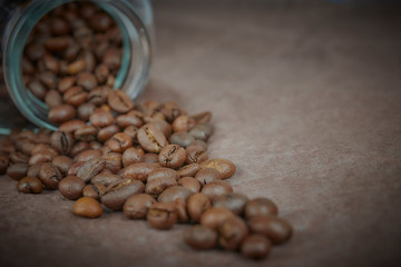 roasted coffee beans poured from a glass jar. angular placement of the coffee object. on dark concrete. horizontal view. copy space