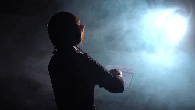 Professional playing the violin in a dark studio with a lantern . Black smoke background. Back view