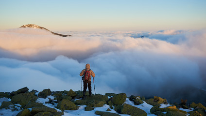 Back view of tourist hiker with backpack and hiking sticks on rocky mountain on background of...