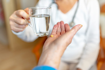 Pflegekraft reicht Rentnerin ein Glas Wasser für die Medikamente