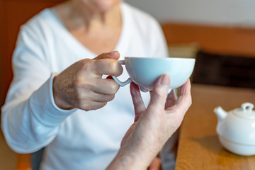 Rentnerin bekommt von der Pflegekraft eine Tasse Tee gereicht