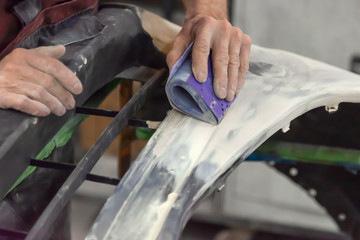 Preparation for painting a car element using sandpaper and putty by a service technician leveling out before applying a primer after damage to a part of the body in an accident.