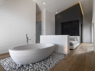 Fototapeta na wymiar in the foreground the modern free-standing bathtub on small white stones in the bedroom the floor is made of wood