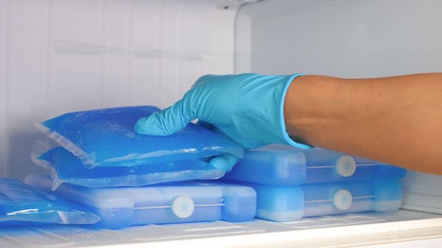 A woman in blue rubber gloves takes an ice pack from the refrigerator. Slow motion. Close up.