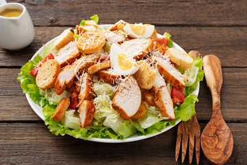 Caesar salad with chicken breast on dark wooden background