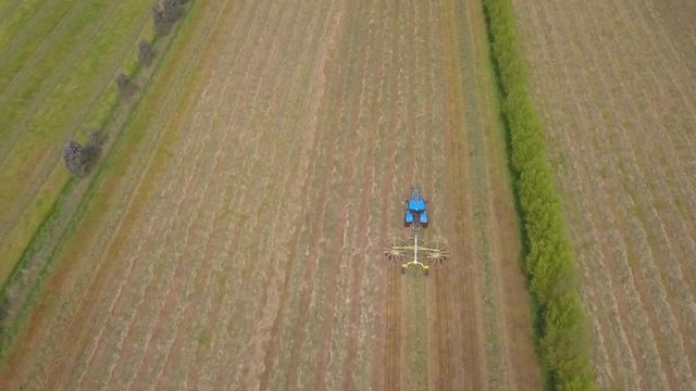 Rising aerial shot of tractor racking hay into rows to prepare for baling on a Waitepeka, New Zealand, farm.