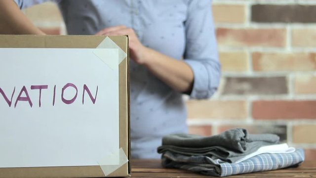 Volunteer is puting clothes to cardboard box for donation