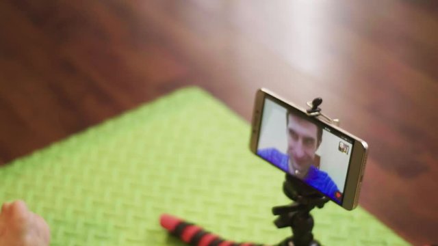 Little boy sitting on the floor is skyping on video call in a smartphone on tripod with his father. 4K slow mo