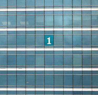 The mumber One on the building's window. The glass facade of skyscraper with many identical windows and one window with sign 1.