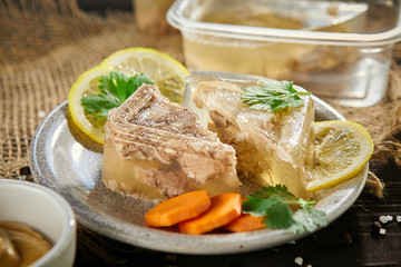 slices of meat jelly with carrots and lemon in a plate on a  on sackcloth  wooden table. Free space for text.close-up