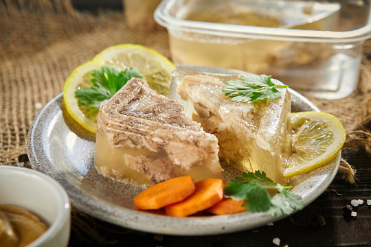 slices of meat jelly with carrots and lemon in a plate on a  on sackcloth  wooden table. Free space for text.close-up