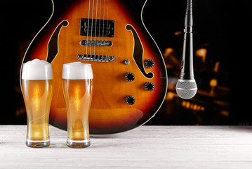 Two glass beer and microphone near electric jazz guitar on white wooden desk. Dark background
