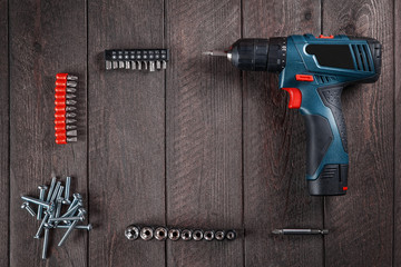 Blue electric screwdriver lies on  black wooden table with bolts and bits. Top view. Free space for text