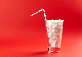 glass with sugar cubes and drinking straw on a red background