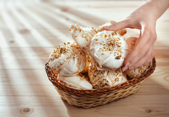 female hand takes  meringue from basket on  wooden table. bright morning. closeup